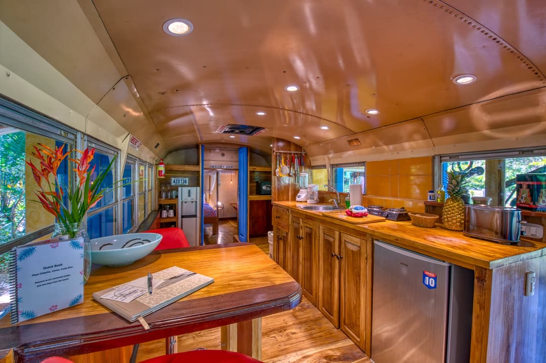 Covered outdoor terrace beside the bus at night — flame hot tub, BBQ, lantern light
